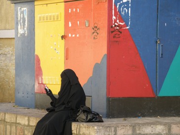 zwartgeklede vrouw (met mobiel) bij veelkleurige keet